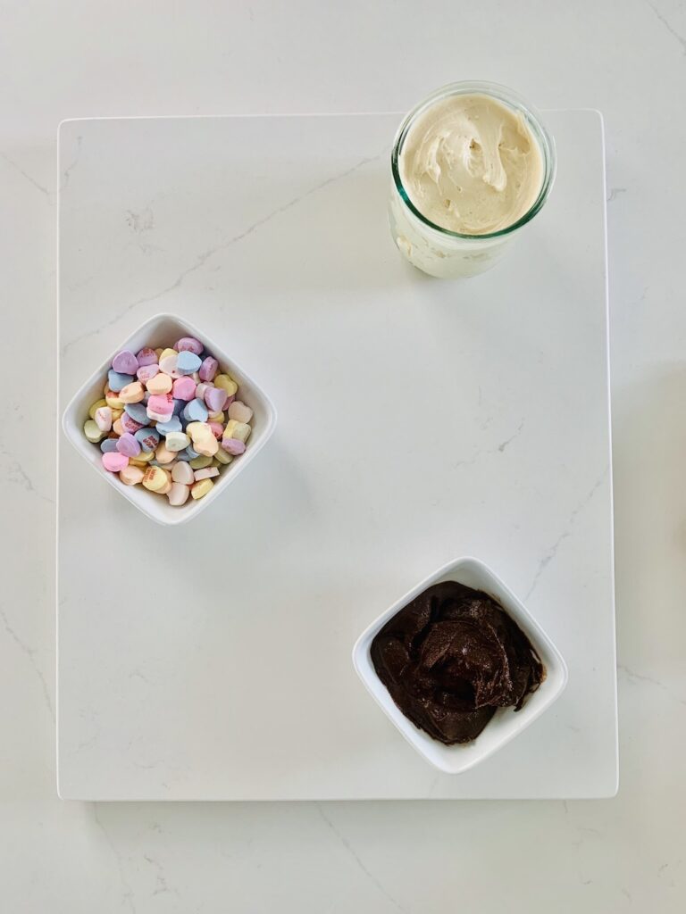 Birds Eye View: Gluten-Free Dessert Charcuterie Board with: cream cheese caramel dip, chocolate dip and candy hearts, in spaced out bowls.