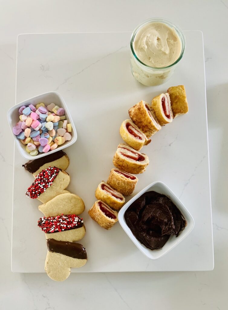 Birds Eye View: Gluten-Free Dessert Charcuterie Board with: cream cheese caramel dip, chocolate dip and Valentine sprinkled heart cookies, candy hearts, and strawberry rugelach.