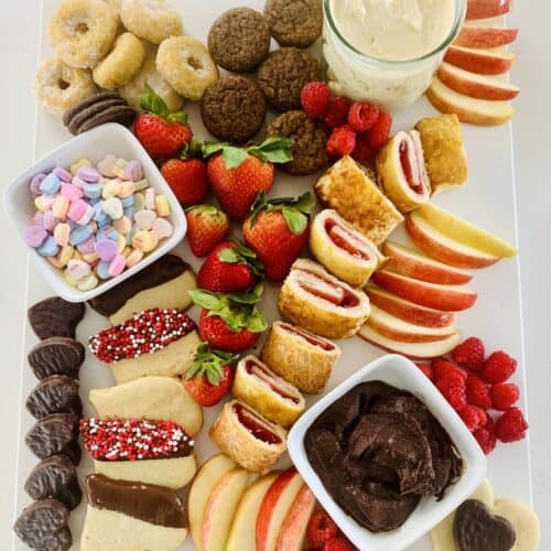 Birds Eye View: Gluten-Free Dessert Charcuterie Board with: donuts, muffins, sliced apples, cream cheese caramel dip, strawberries, candy heart, chocolate dip and Valentine sprinkled heart cookies, candy hearts, raspberries and chocolate hearts.