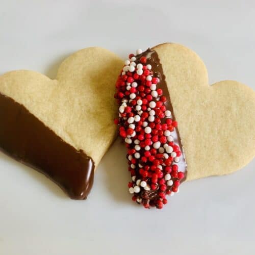 2 heart cookies with one edge dipped in chocolate. One also has been dipped in red white and pink sprinkles.