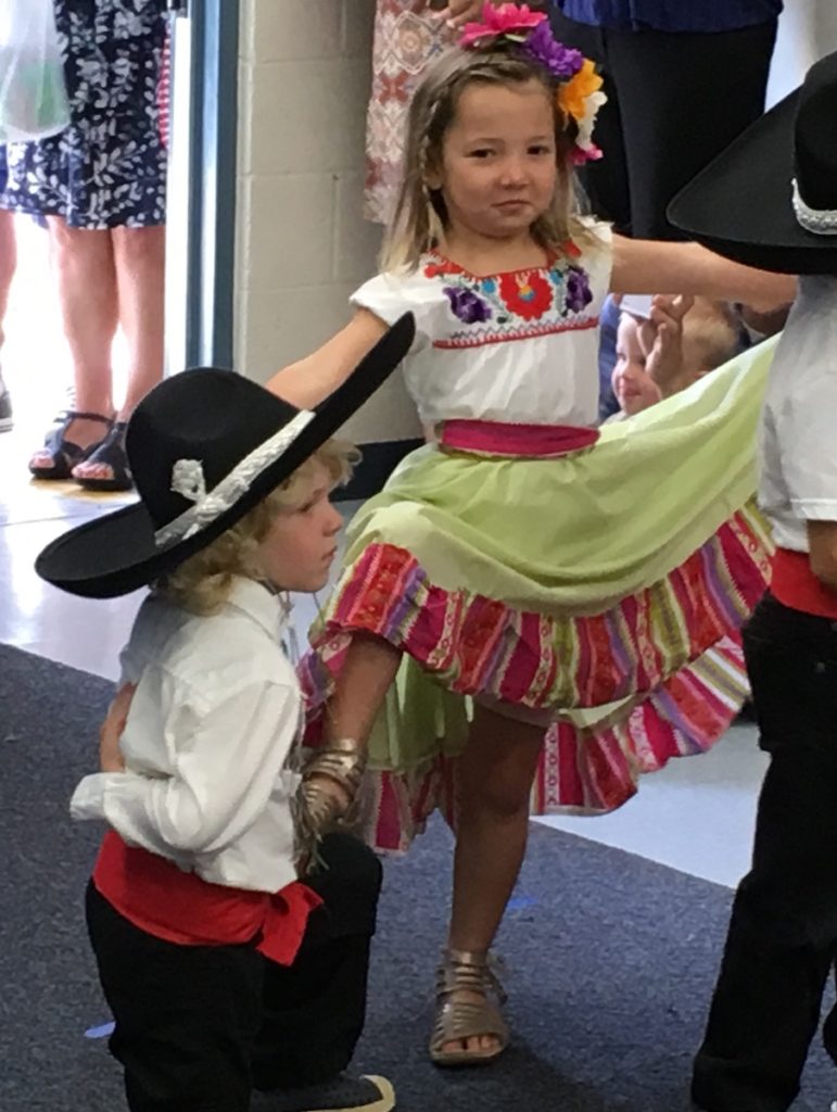 Miss E wearing a Mexican dress and performing a dance at her Spanish-language preschool