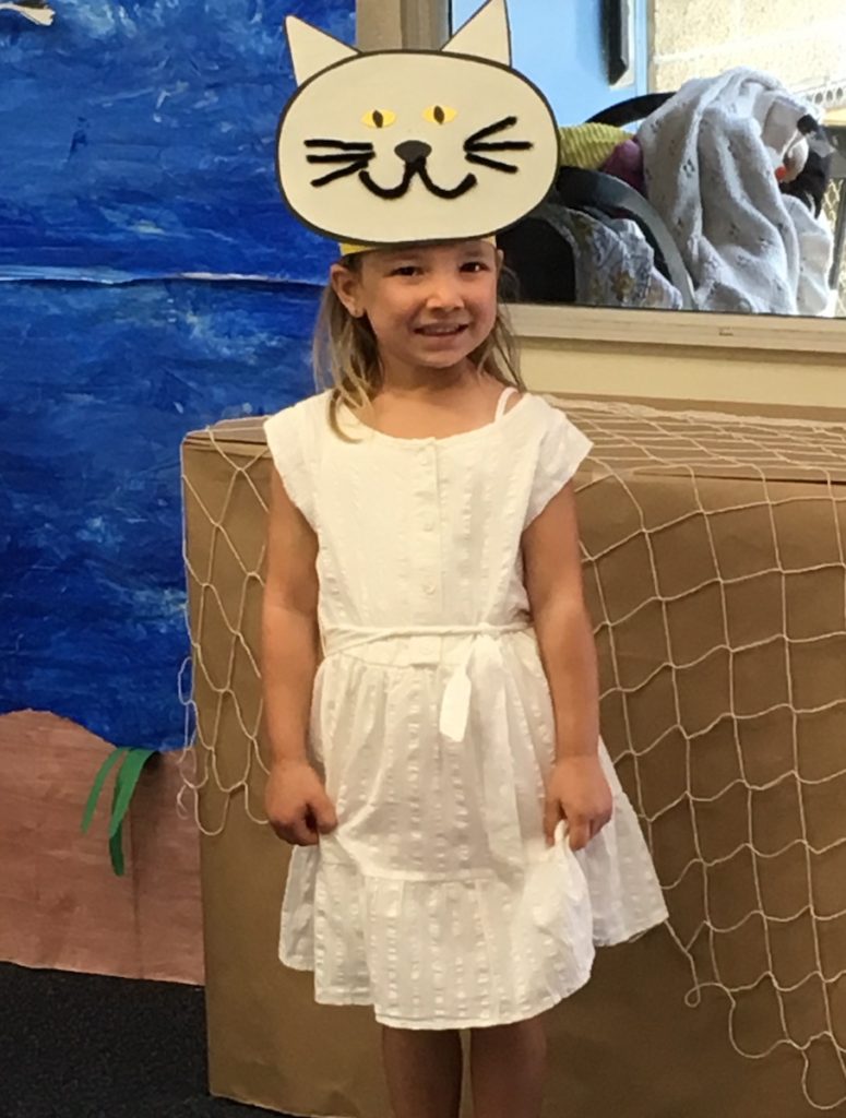 Miss E wearing a cat "hat" on her head and a white dress