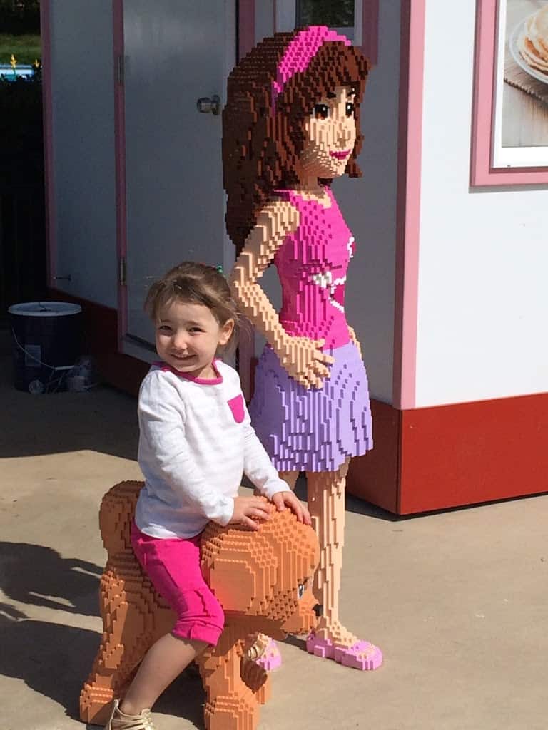 Miss E enjoying a gluten-free trip to Legoland, smiling while riding a Lego dog next to a Lego friends character
