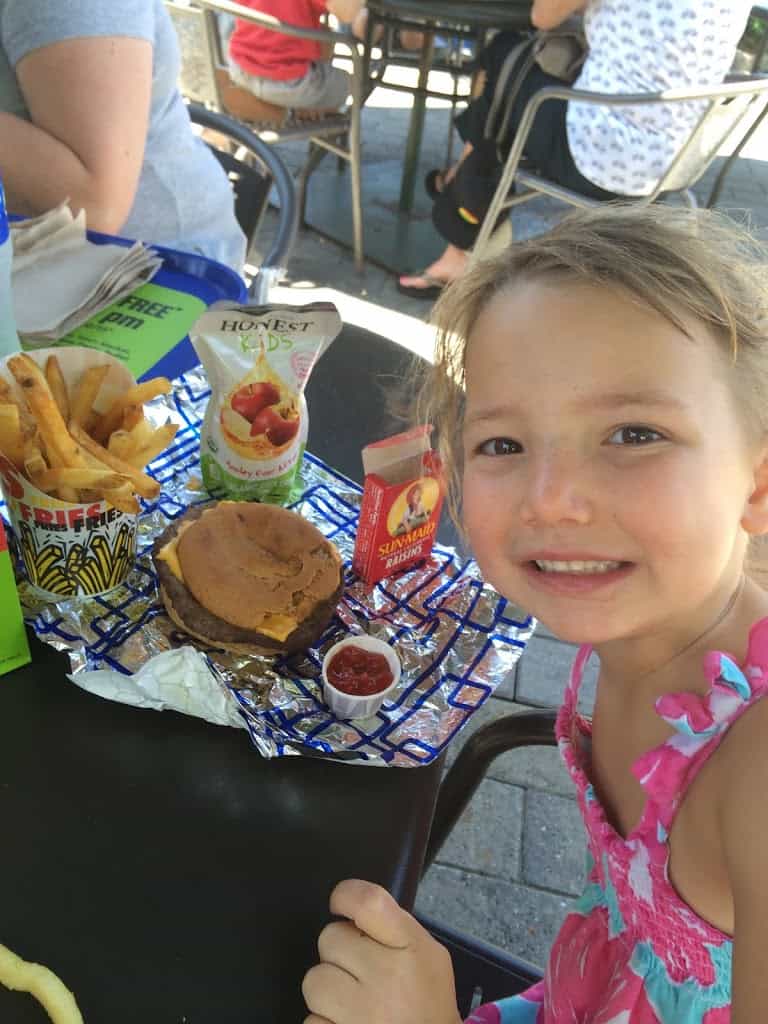 Miss E smiling in front of her gluten-free meal at the Burger Stop: gluten-free cheeseburger, fries, juice and raisins