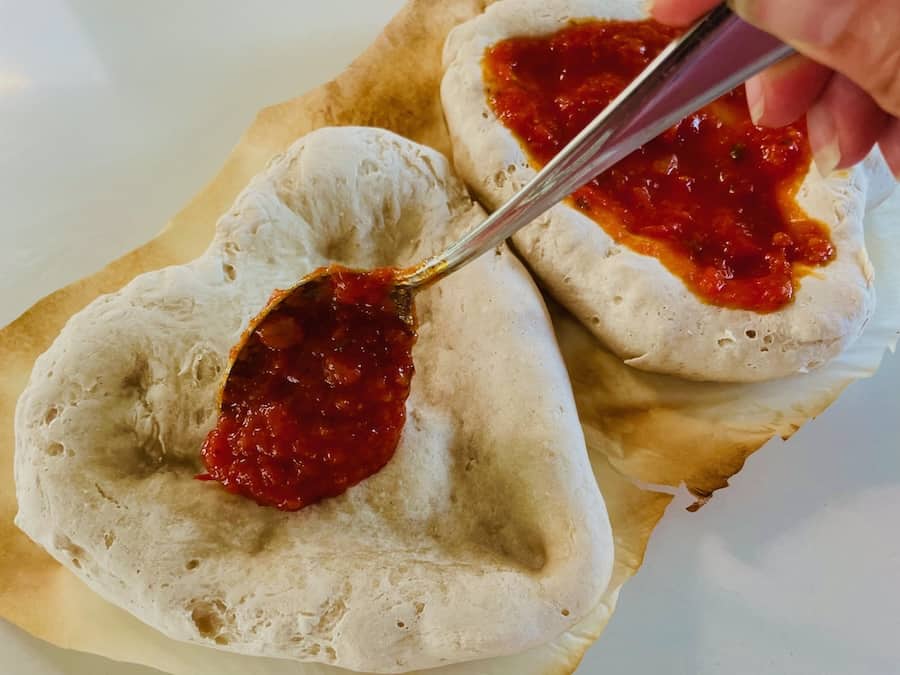 Red sauce being placed on two heart-shaped pizza crusts.