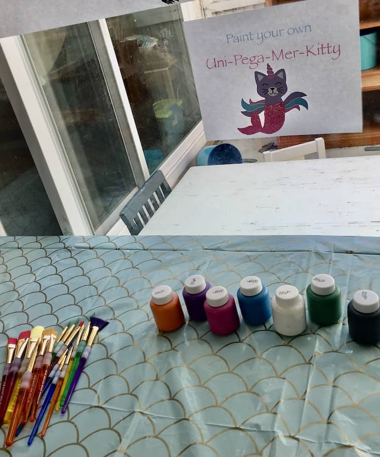 table with paint and brushes under a sign that says "paint your own uni-pega-mer-kitty"