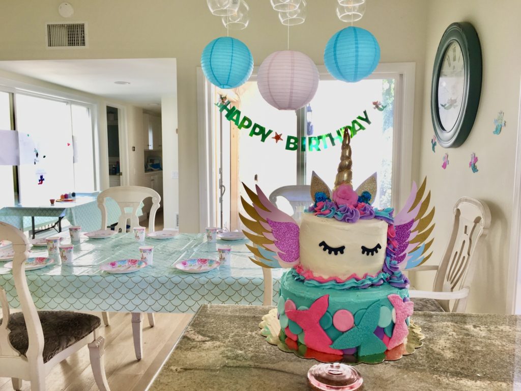 unicorn-pegasus-mermaid-kitten gluten-free birthday cake in the foreground with decorated party table and Happy Birthday banner in the background