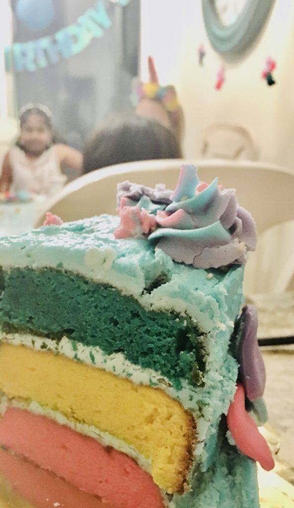 a slice of gluten-free birthday cake showing the three colored layers, aqua, yellow and pink