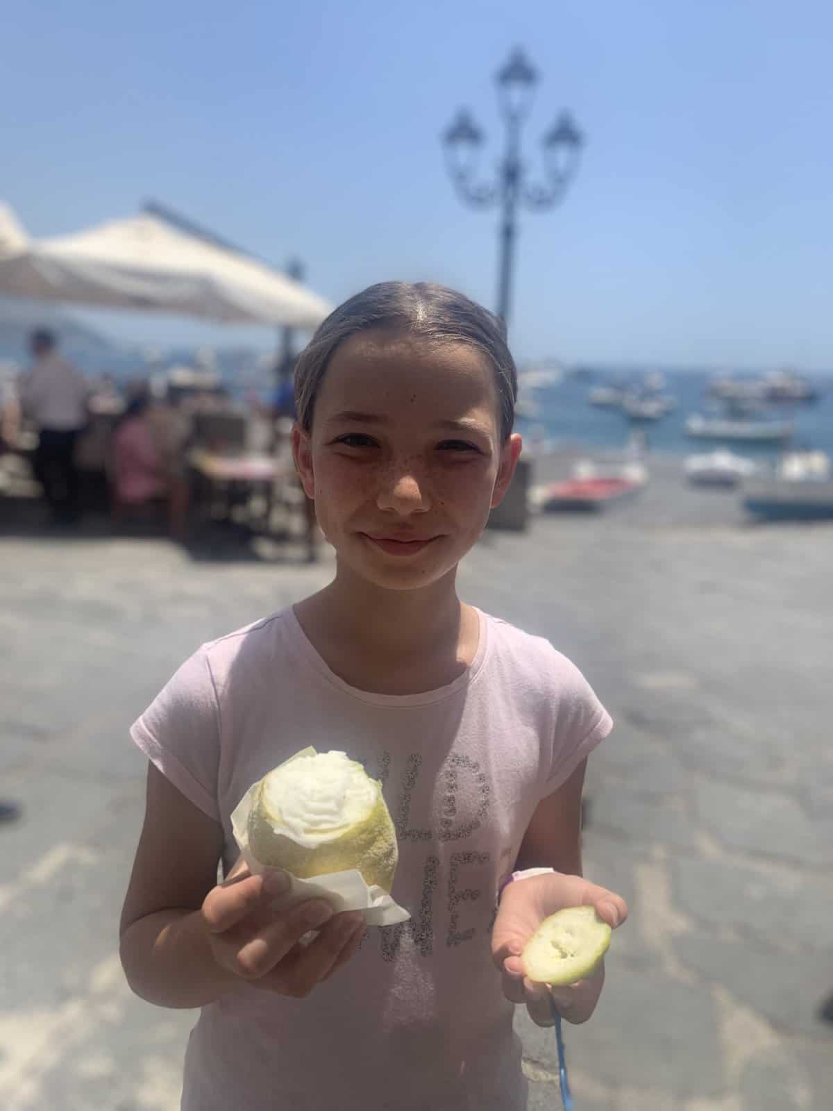 Miss E holding a gluten-free lemon gelato inside a lemon in one hand and the lemon "lid" in the other