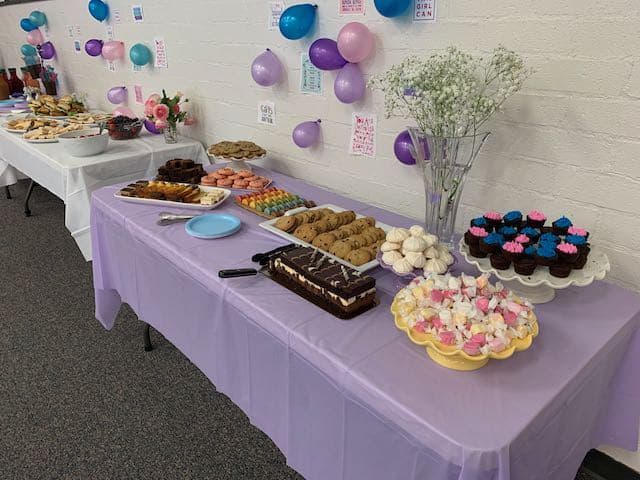 two tables with desserts and tea sandwiches, the first table is covered with a purple tablecloth, the one in the background has a white tablecloth