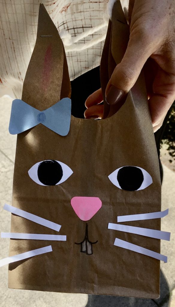 Easter bunny with blue bow, pink nose and white whiskers, made of a brown, paper lunch bag and construction paper