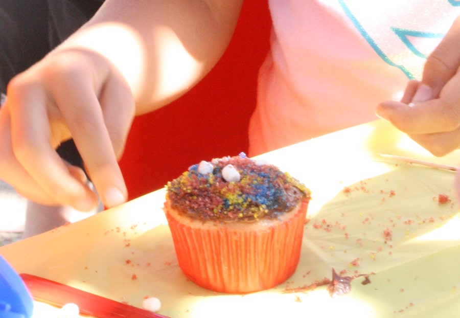 child's hand adding sprinkles to vanilla cupcake with chocolate frosting
