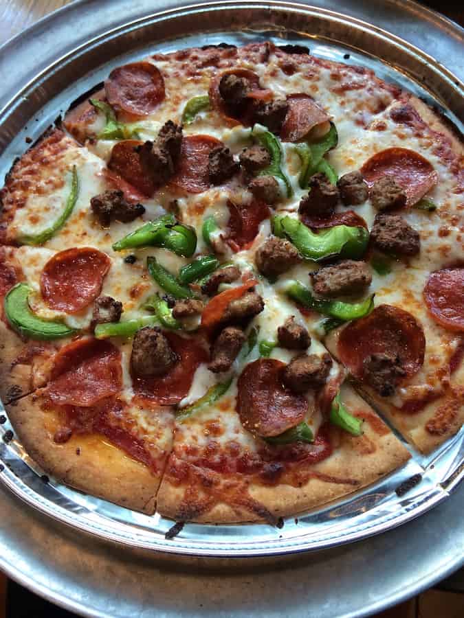 gluten-free pizza with pepperoni, green peppers and sausage, cut into four slices and served in its own tin