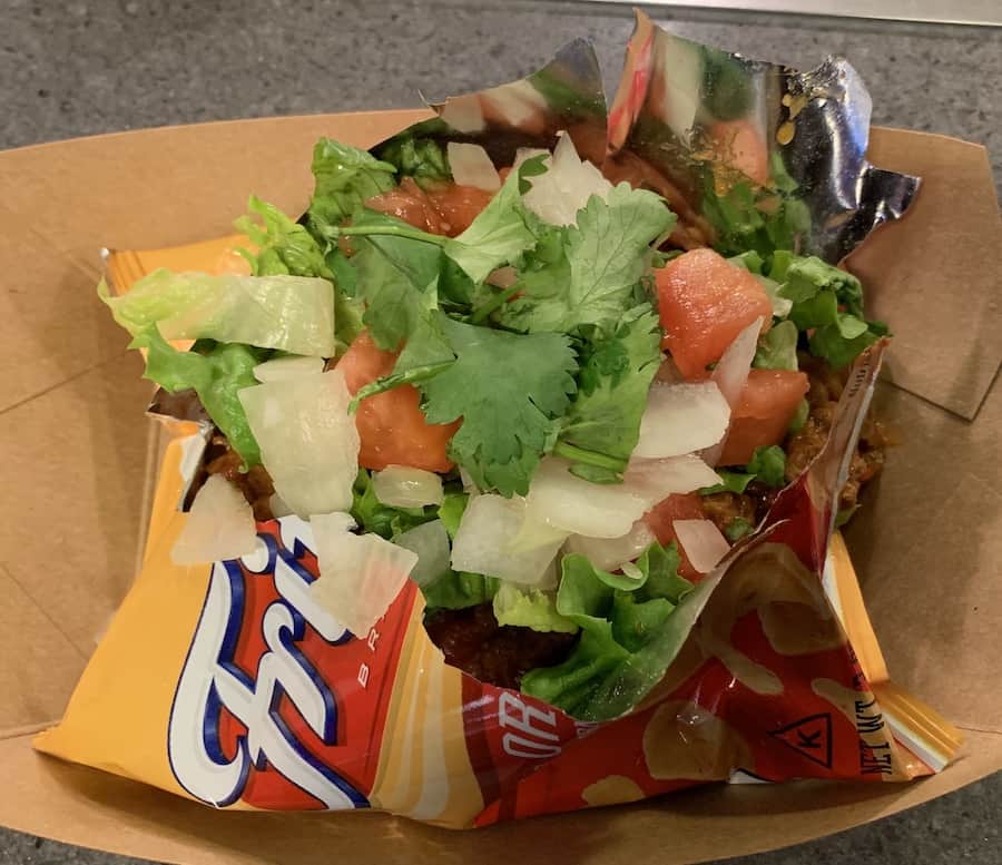 cut open Fritos bag with meat, onion, cilantro, cheese and tomato