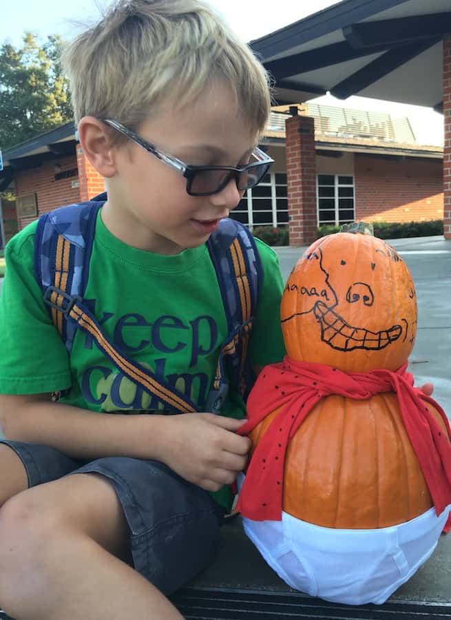 CJ looking at "Captain Underpants, made of two pumpkins, one is the head with a face drawn in marker, the larger, bottom pumpkin is the body wearing a red cape and white underwear 