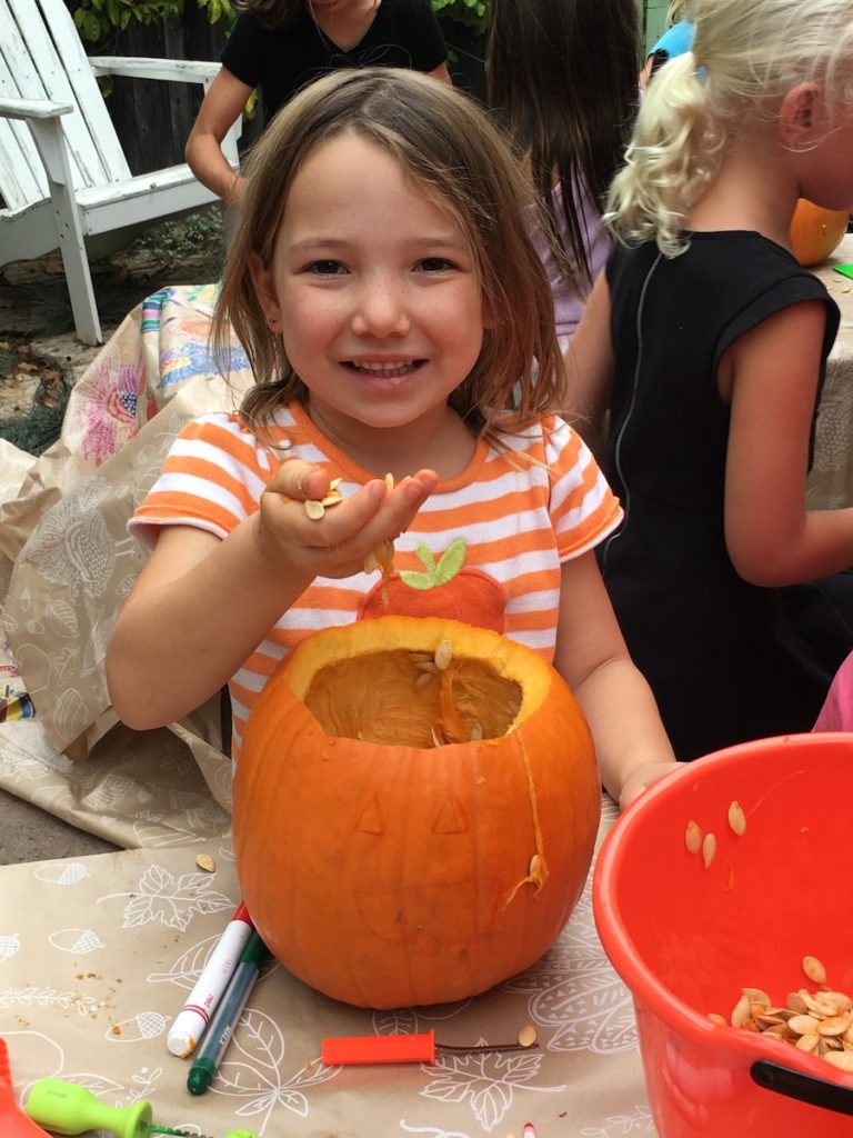 Miss E smiling while holding seeds she just scooped out of a Pumpkin