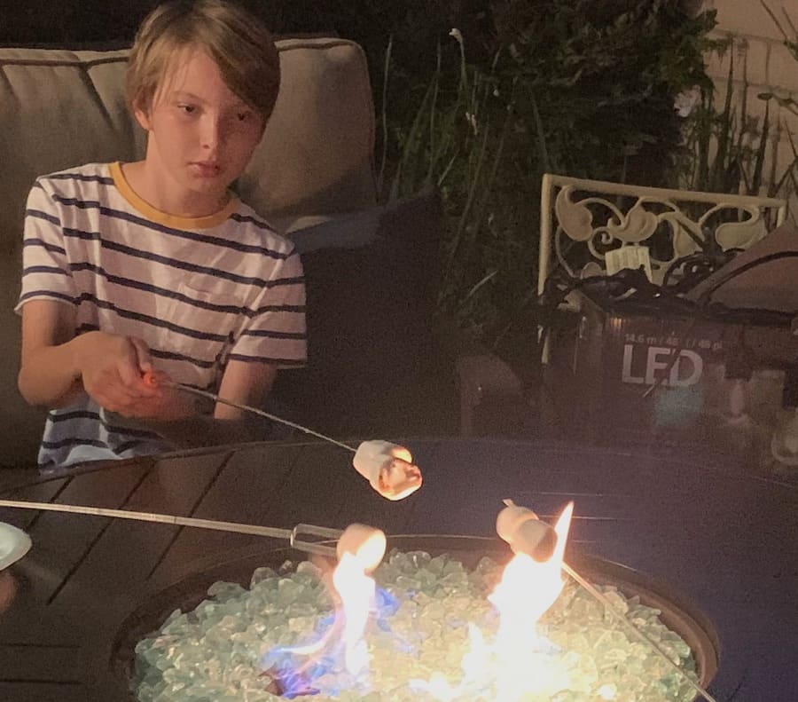 boy in striped shirt roasting a marshmallow over an outdoor fire pit