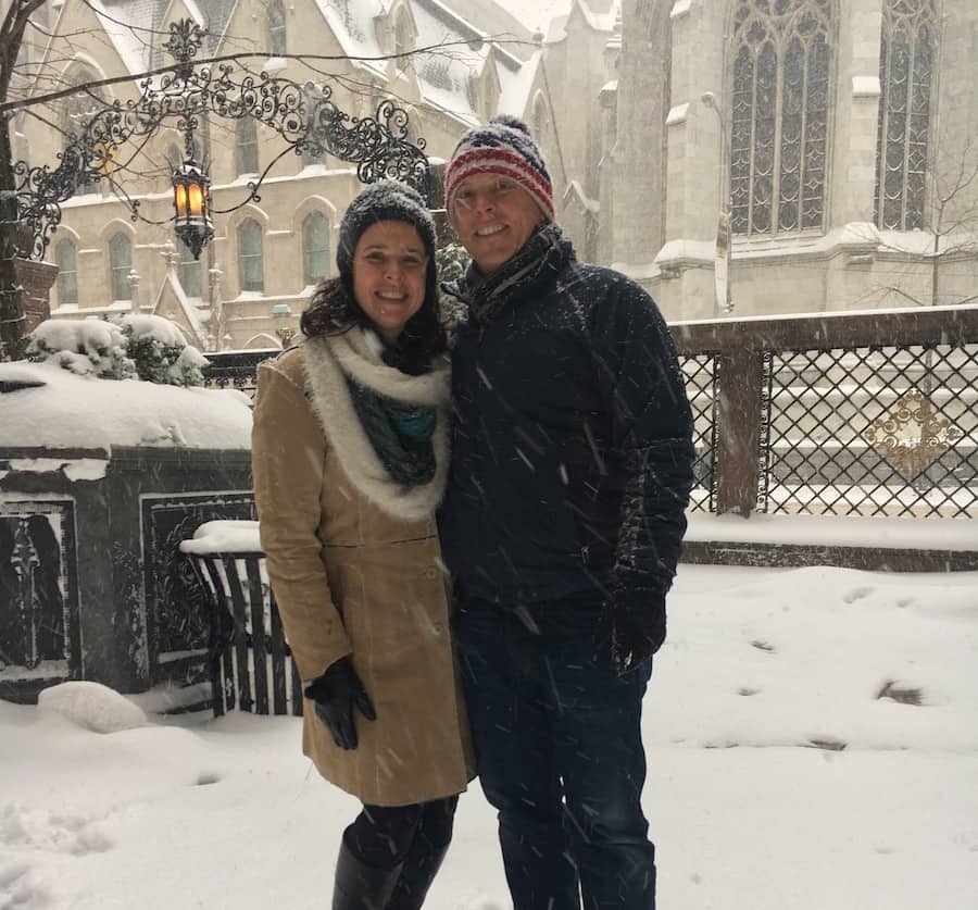 Dave & Heather in winter coats and hats smiling in a snow covered courtyard with St. Patrick's Cathedral in the background