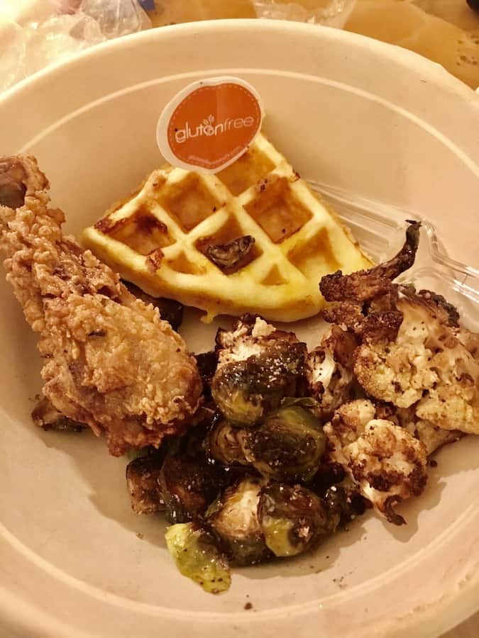 plate with gluten-free fried chicken, gluten-free cheddar waffle wedge, roasted cauliflower and Brussels sprouts, thee is a food pick in the waffle wedge with an orange circle and the words "gluten-free" on it