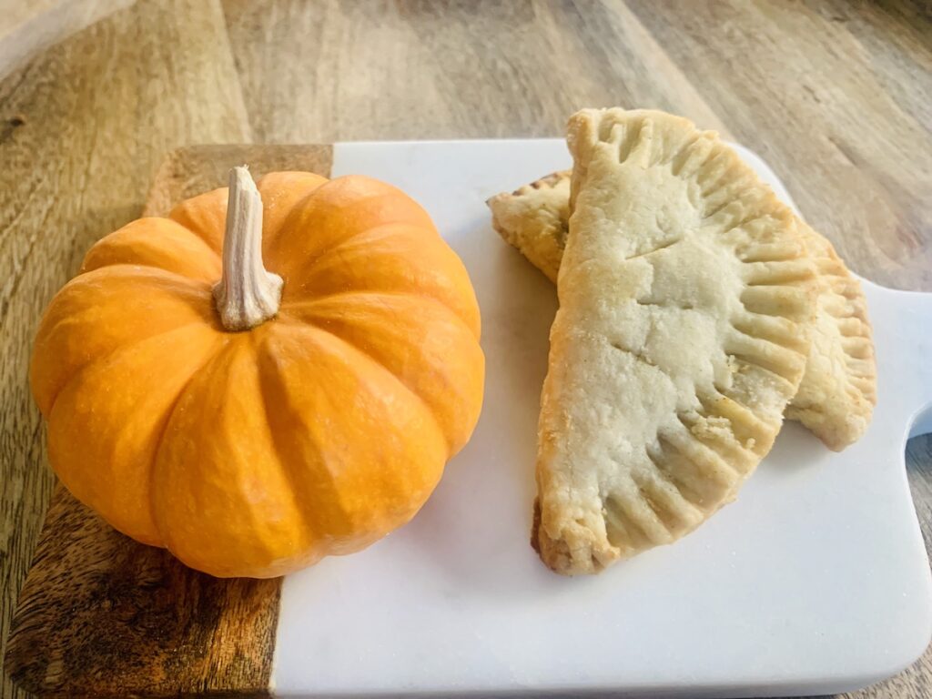 Mini pumpkin and 2 pumpkin pasties with on a cutting board.