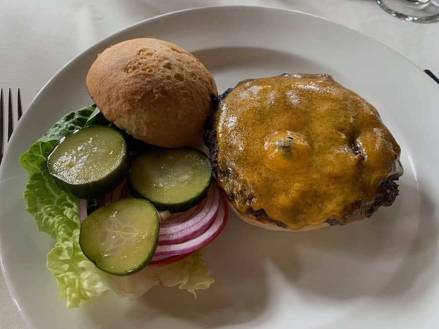 gluten-free cheeseburger from the Ahwahnee Dining Room - top bun is to the left of the cheeseburger with a pile of pickles, red onion and lettuce below