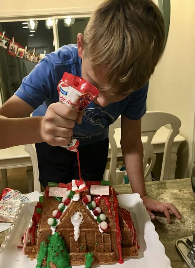 CJ pouring red cake icing to fill the chimney of his gluten-free gingerbread house