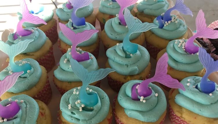 mermaid cupcakes with blue frosting, white pearls, and blue and purple mermaid tail rings as toppers, cupcakes are made with Pillsbury Gluten-Free Funfetti cake mix