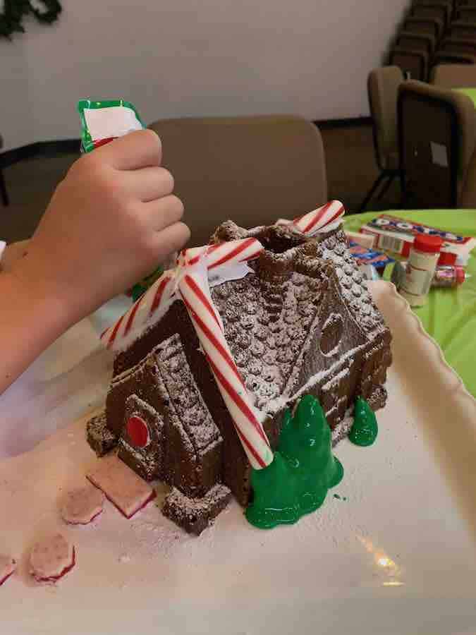 a child's hand squeezing icing onto a gluten-free gingerbread house