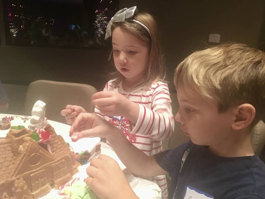 Miss E with a piece of candy in her mouth and CJ, both adding candy to their gluten-free gingerbread house