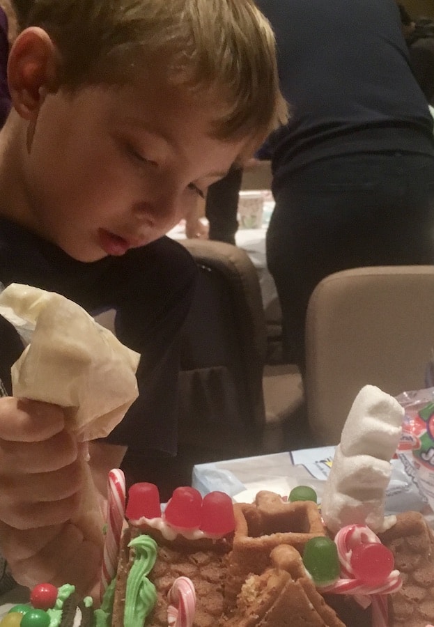 CJ is concentrating while adding white frosting to his gluten-free gingerbread house cake