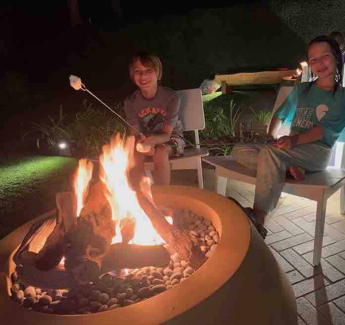 CJ and Miss E sitting in chairs next to a firepit, roasting marshmallows