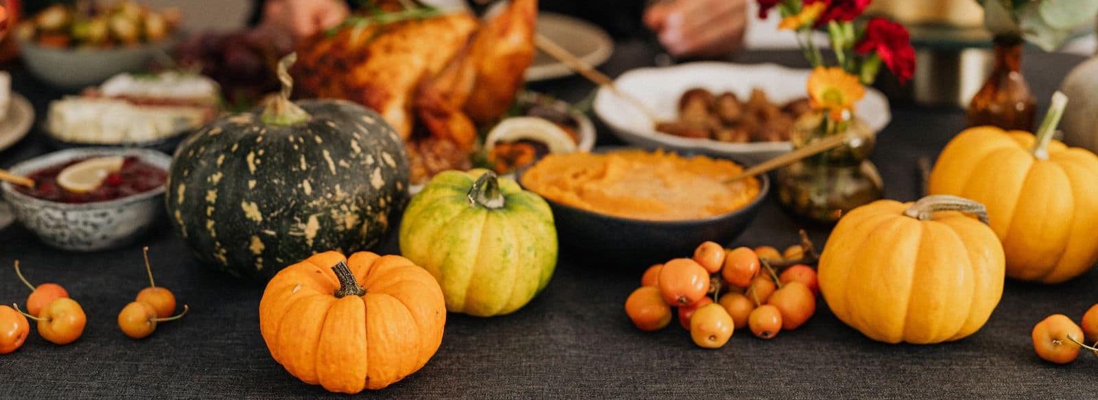 a gluten-free thanksgiving table with pumpkins, cranberry sauce, sweet potatoes, turkey, and indistinguishable, blurred dishes