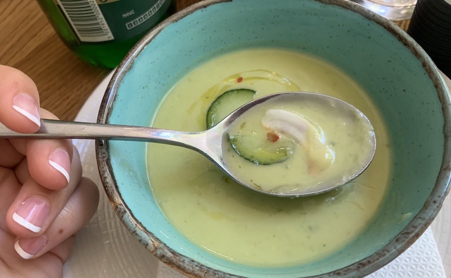 gluten free cucumber soup in a blue bowl with a hand holding a spoonful