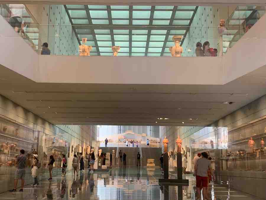 View through an atrium of two stories of the Acropolis Museum, museum visitors and artifacts in the background