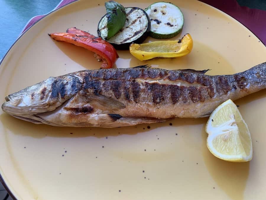 whole grilled fish and vegetables with lemon on a yellow plate