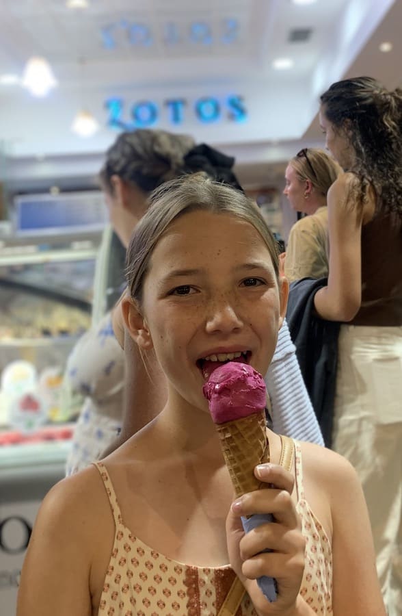 Miss E taking a bite out of her gluten-free berry gelato in a gluten-free cone, the Gelateria Zoro (and its sign) are visible in the background