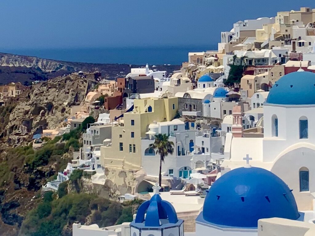 View of the town of Oia, Santorini, cave houses, some with blue domes, and the sea in the distance