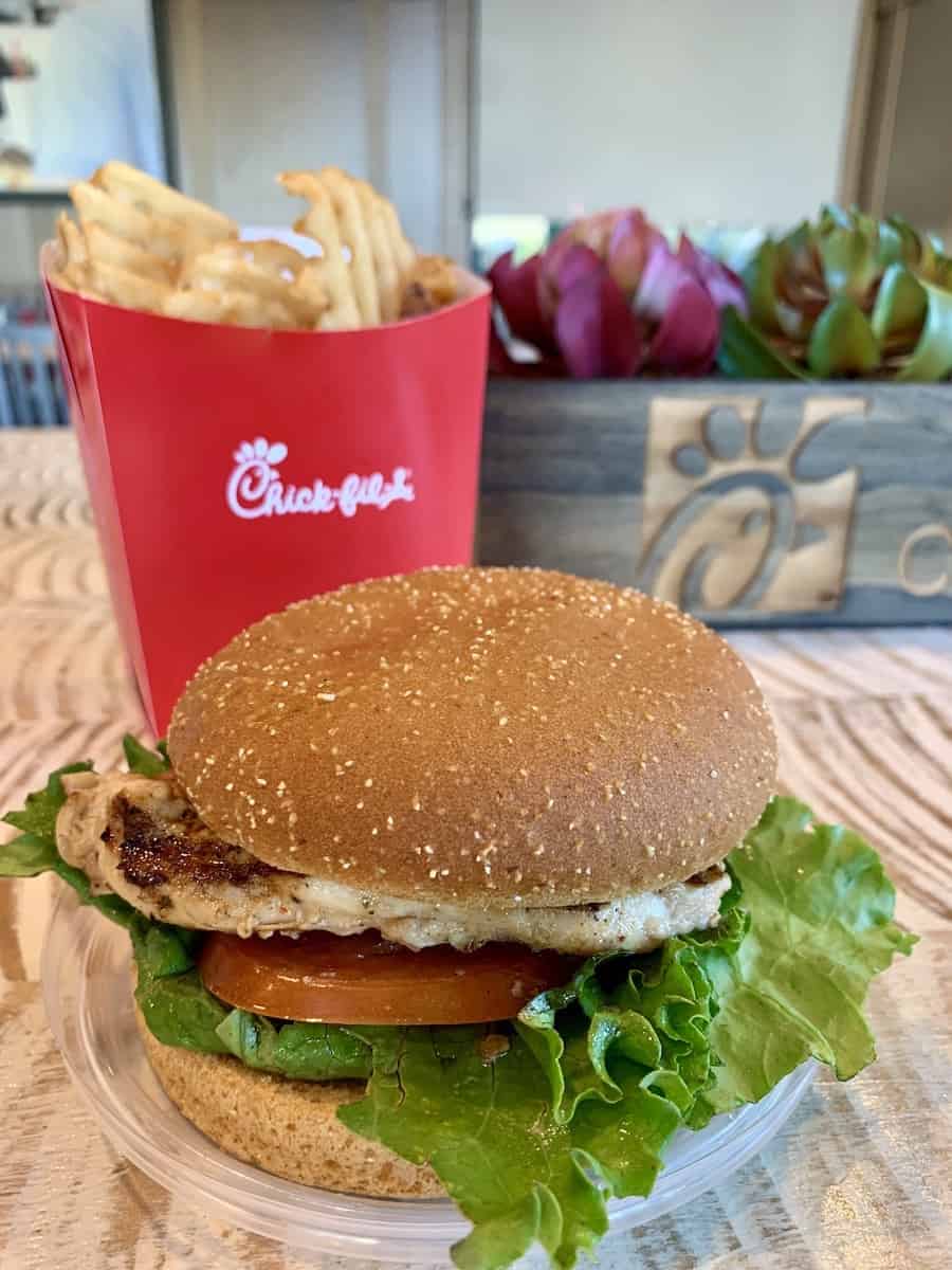 Chick-Fil-A gluten-free grilled chicken sandwich on a gluten-free bun, with lettuce and tomato, gluten-free Chick-fil-A French fries in the background