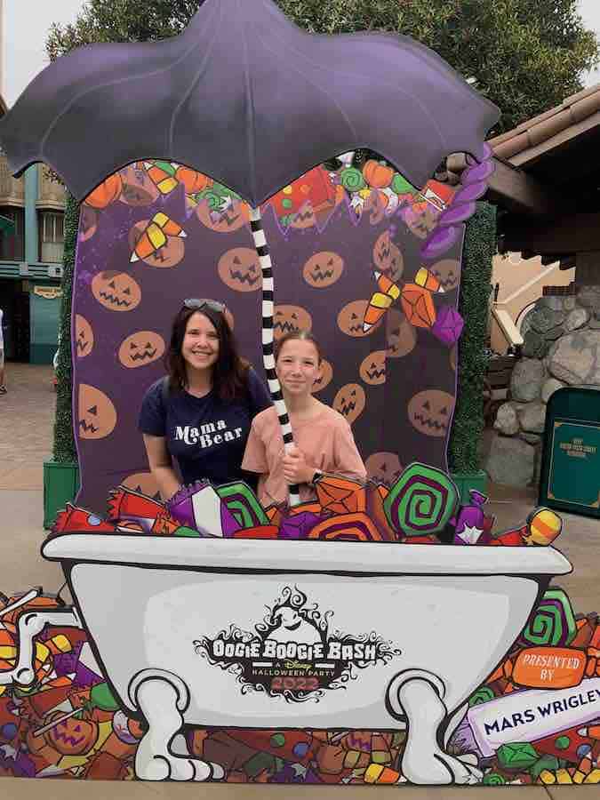 Heather and Miss E smiling in a photo booth, under an umbrella with the appearance of raining pumpkins and candy while they are standing in a bathtub
