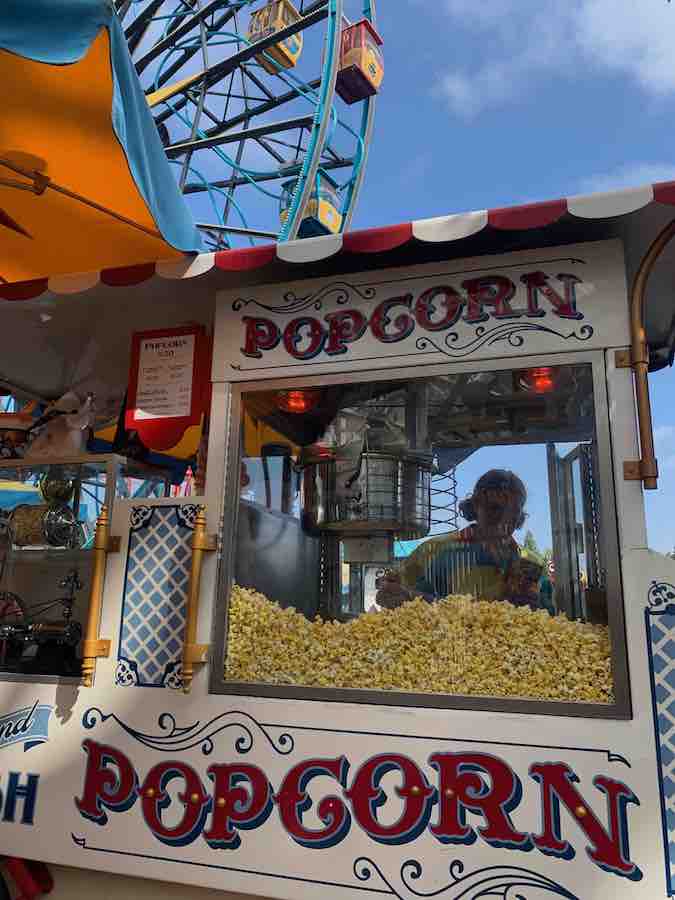 A popcorn cart with a cast member in the background and Ferris wheel in the background above