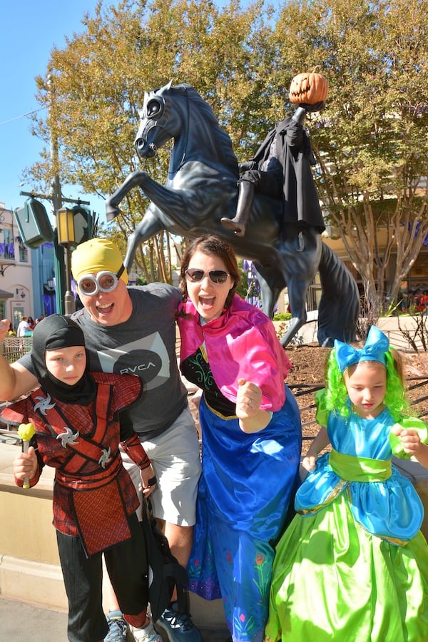 CJ in a ninja costume, Dave with a Minion mask/goggles, Heather in a Princess Anna dress & Miss E in a Drizella dress, all running from the Headless Horseman statue in the background