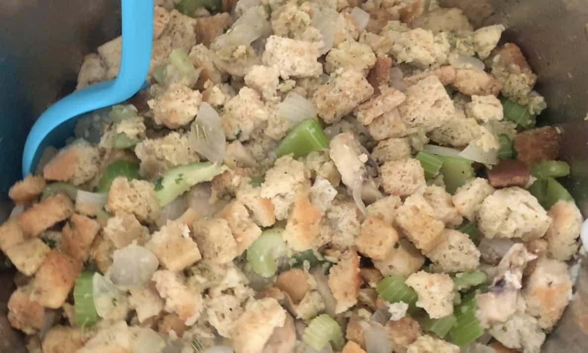 Veggies and stuffing mix in a crockpot with an aqua spoon.