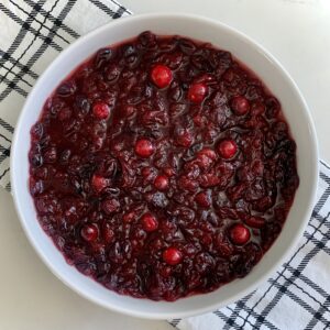 Cranberry sauce in a white bowl on top of a black and white plaid dishtowel.