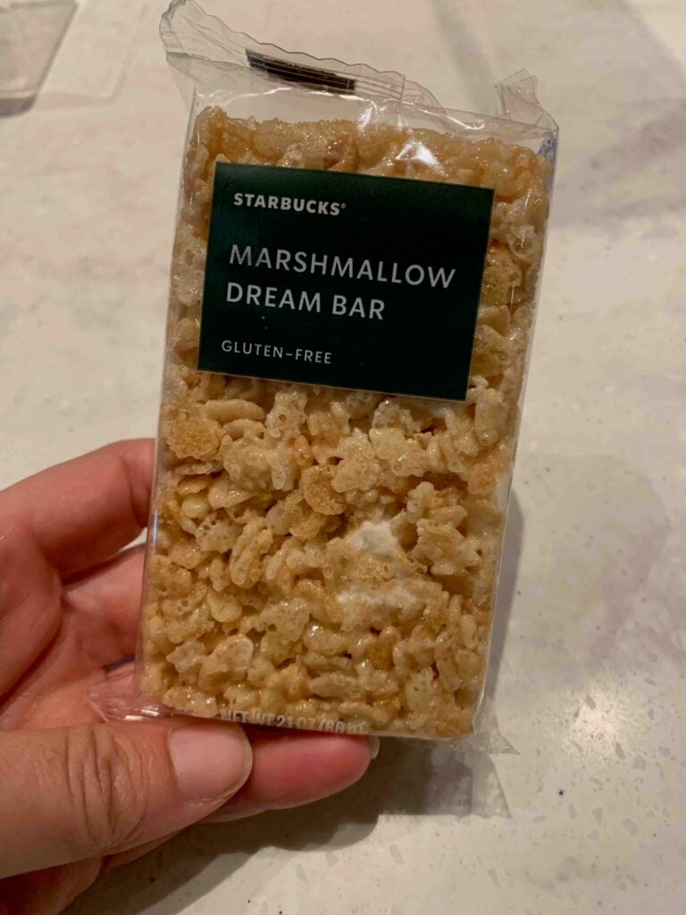 hand holding marshmallow dream bar with green label and white text: "Starbucks Marshmallow Dream Bar, Gluten Free"