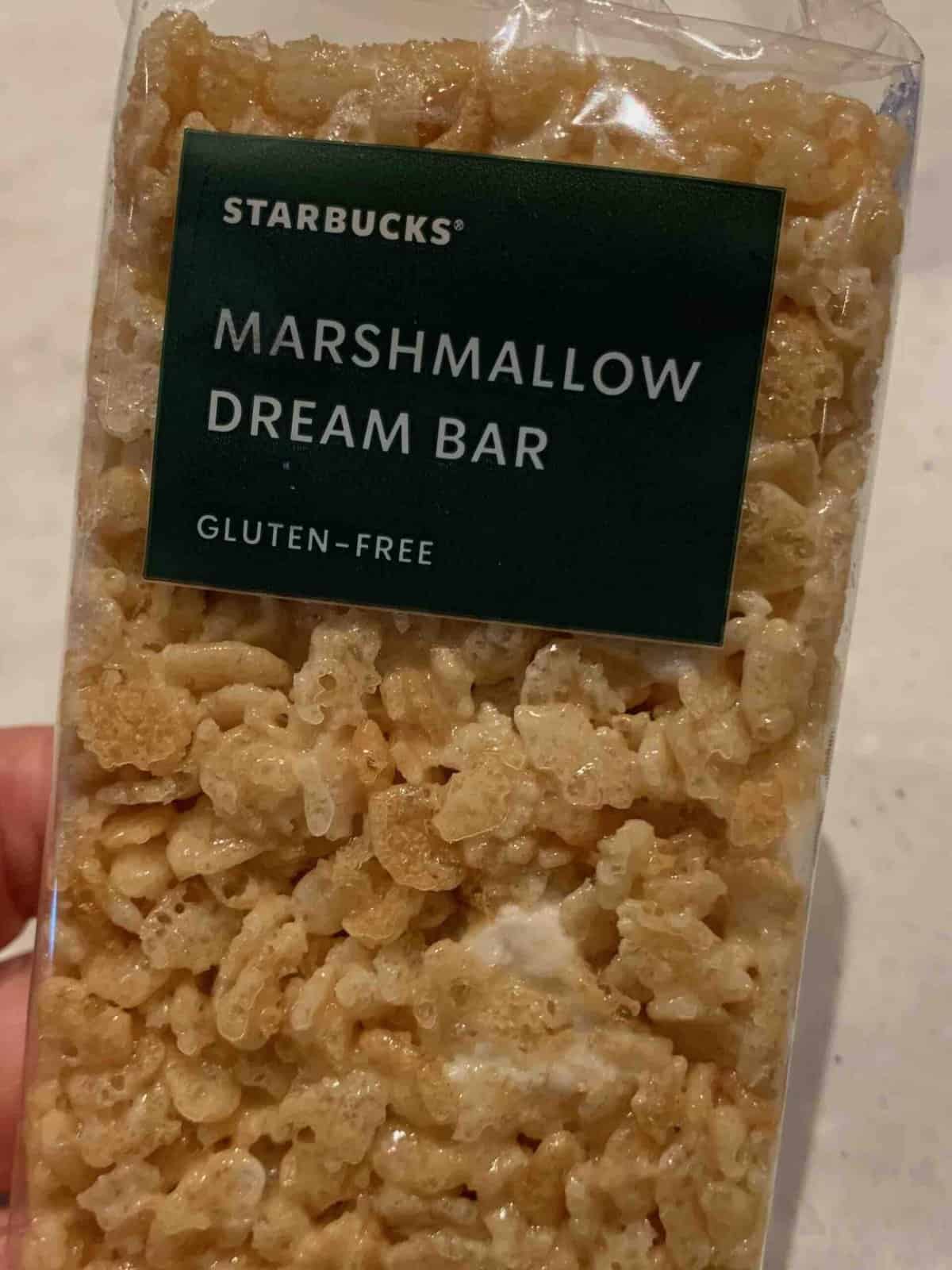 hand holding marshmallow dream bar with green label and white text: "Starbucks Marshmallow Dream Bar, Gluten Free"