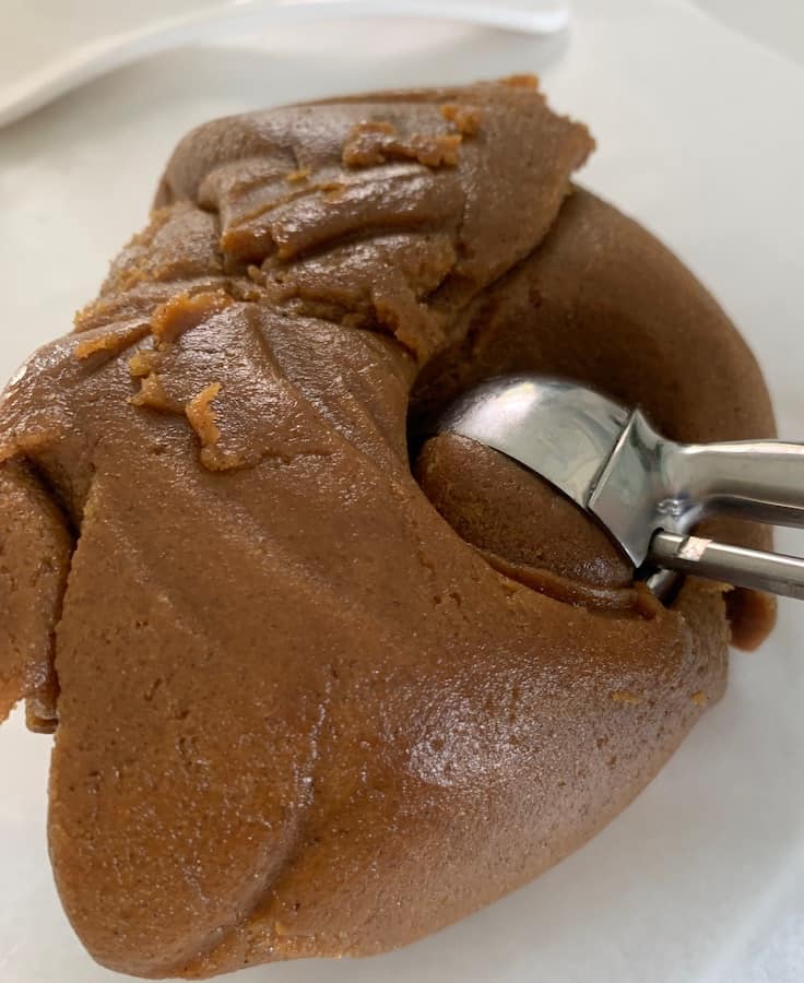 cookie dough scooper scooping out of a ball of gluten-free gingersnaps cookie dough