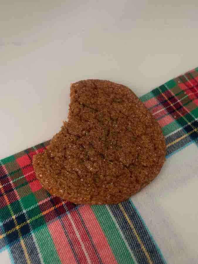 gluten-free gingersnap with a bite missing, on a plaid Christmas fabric