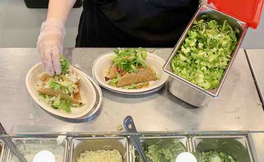 Chipotle employee adding romaine lettuce from a separate, clean container to gluten-free crispy tacos