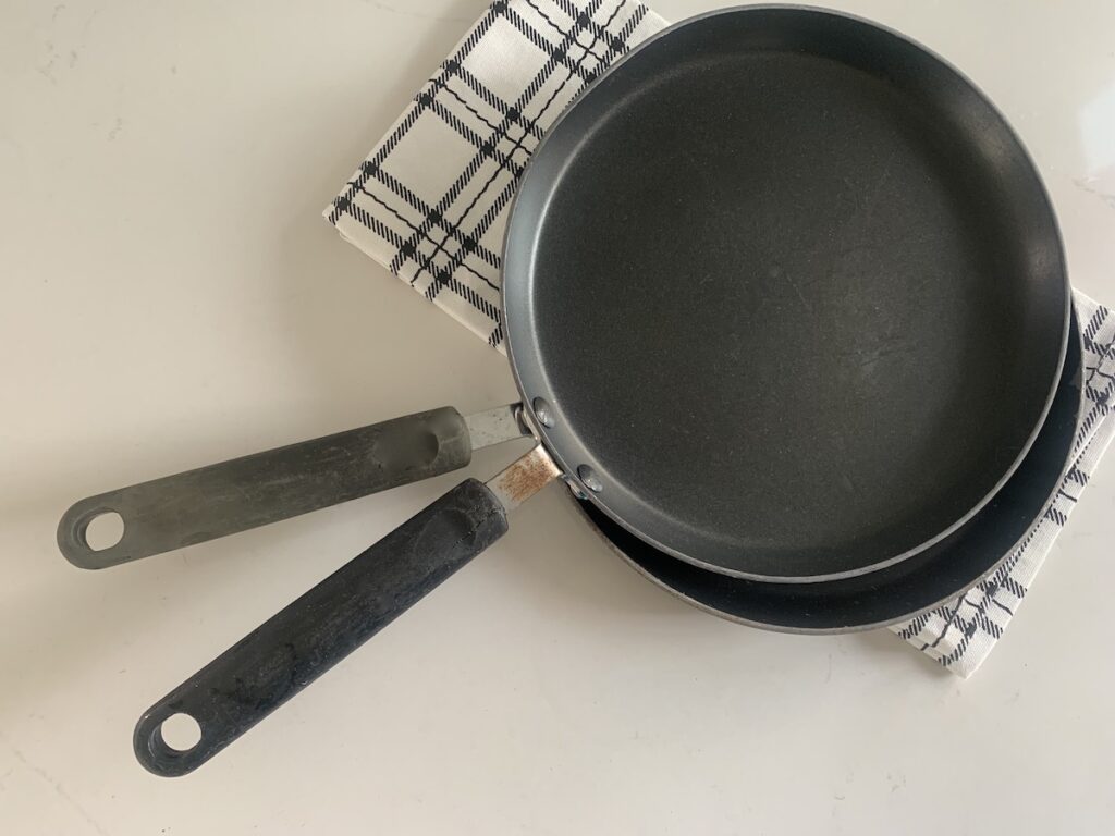 Bird's eye view: 2 crepe pans on top of a black and white plaid dish towel. 