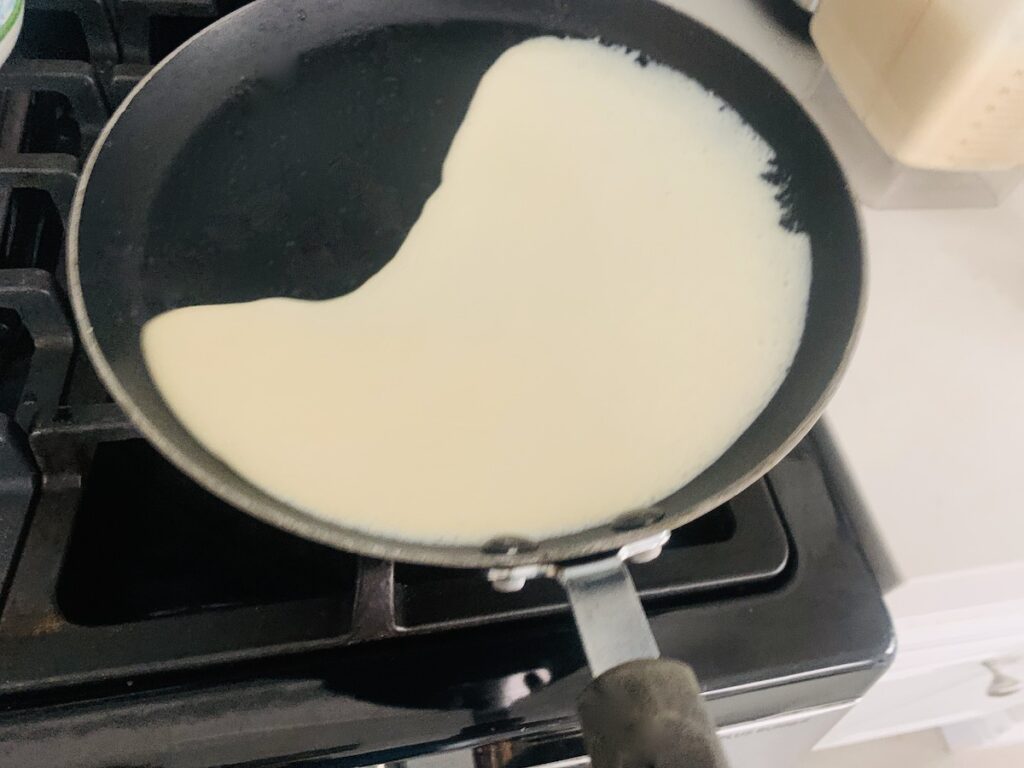 Crepe batter being tilted around a crepe pan, not all the way around yet, as part of the pan does not have batter.